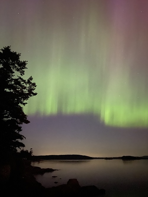 The aurora borealis (northern lights) light up the sky over the water in a stunning green.